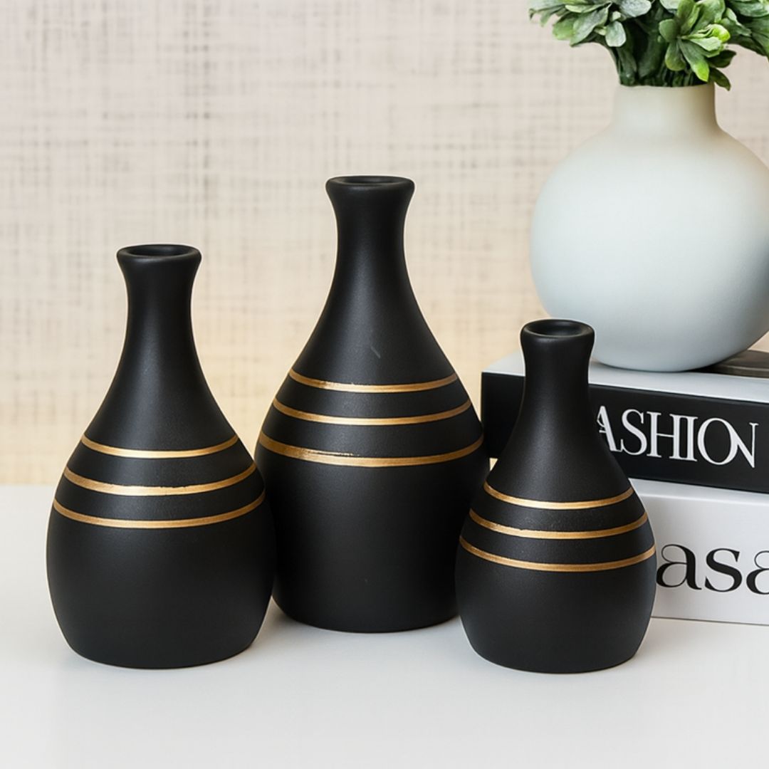 Trio de vasos de cerâmica pretos com listras douradas sobre livros decorativos

