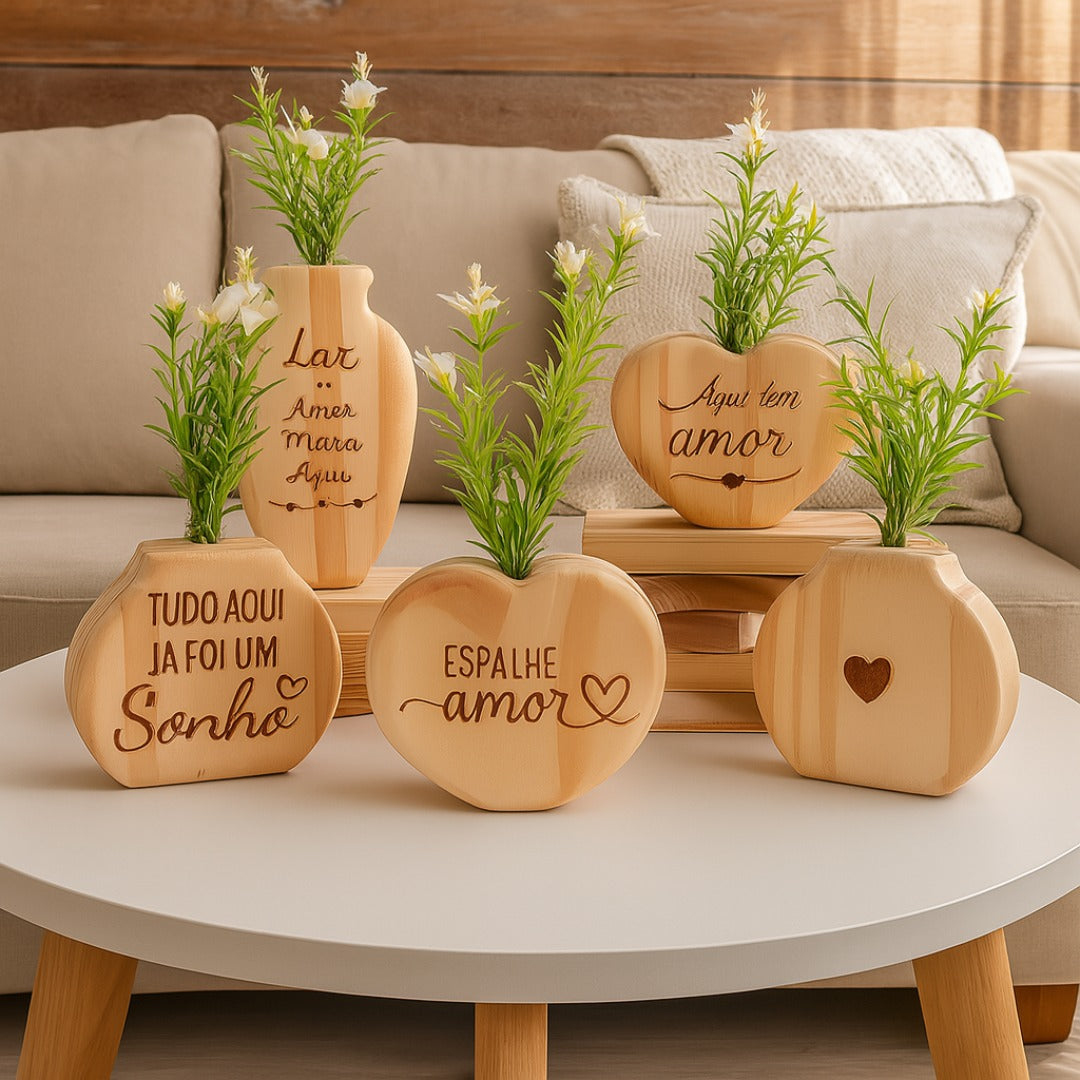 Vasos decorativos em madeira com frases gravadas e flores artificiais, sobre mesa redonda em ambiente aconchegante

