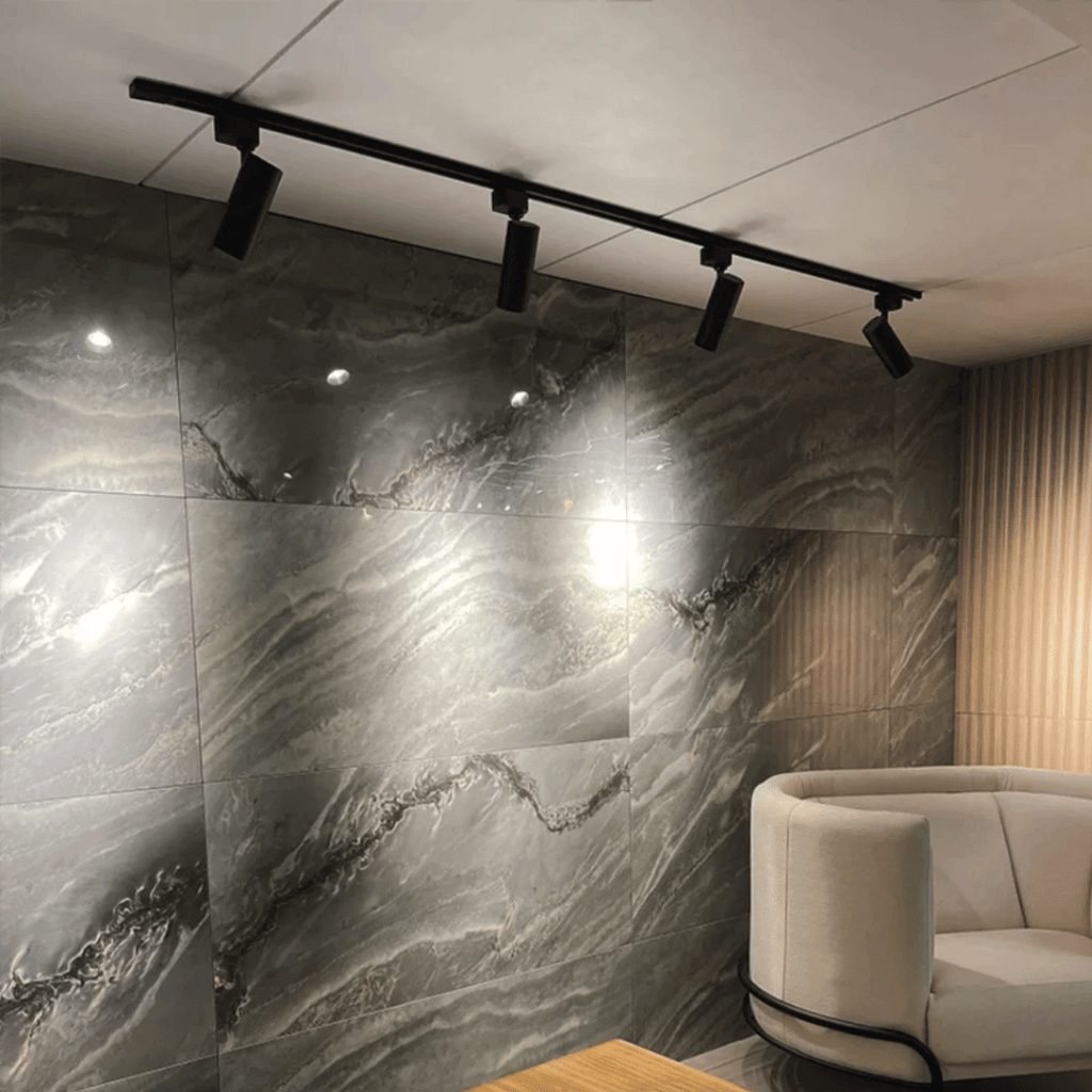 Trilho preto instalado com 4 spots iluminando parede texturizada

