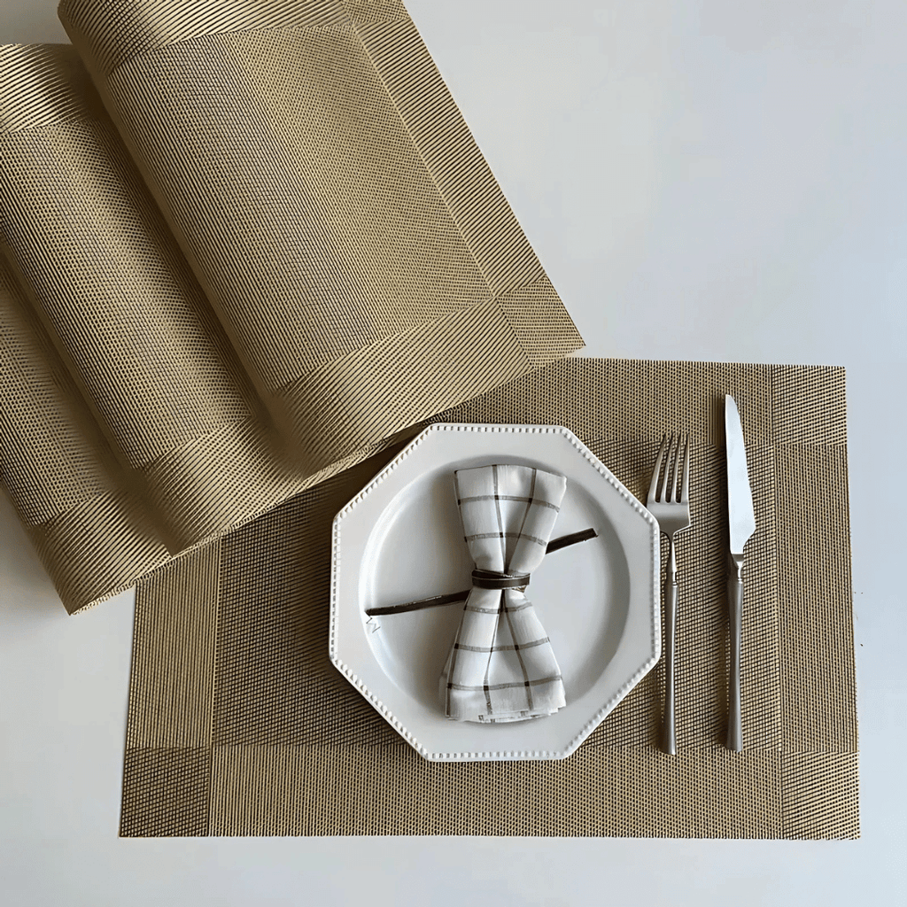 Jogo americano dourado com prato branco e talheres inox sobre mesa clara

