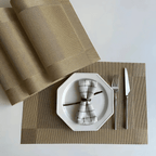 Jogo americano dourado com prato branco e talheres inox sobre mesa clara

