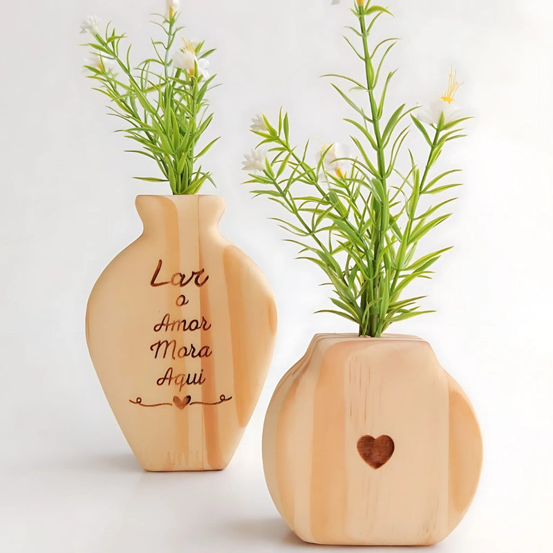 Dois vasos decorativos de madeira clara com flores artificiais, um com a frase "Lar o Amor Mora Aqui" e outro com coração vazado

