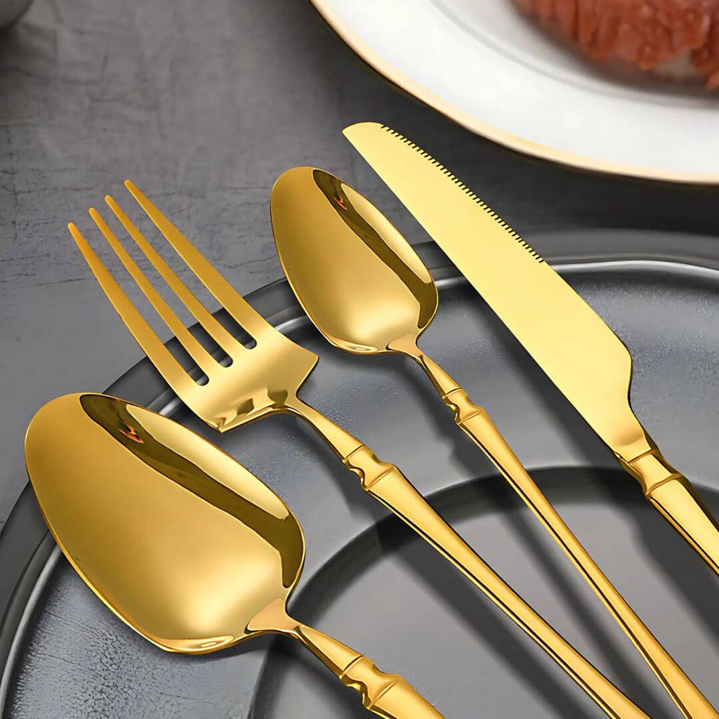 Conjunto de talheres Vesta com acabamento dourado sobre prato cinza

