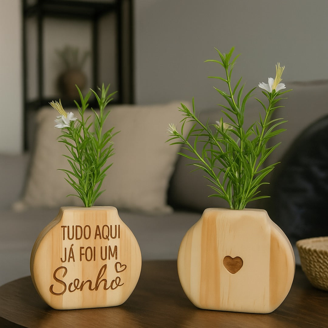 Vaso com a frase "Tudo aqui já foi um sonho" e vaso com coração entalhado, sobre mesa de madeira em ambiente moderno

