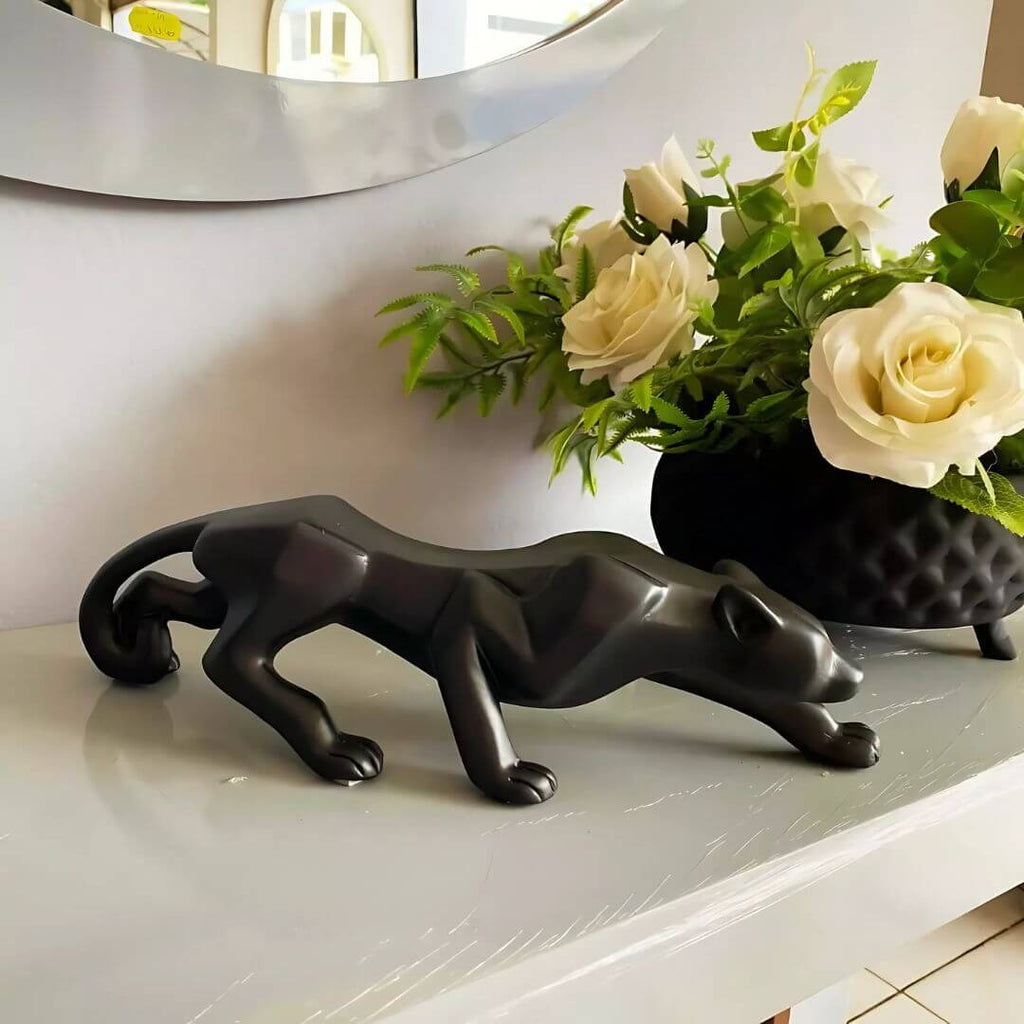 Enfeite pantera preta em destaque sobre aparador com plantas ao fundo

