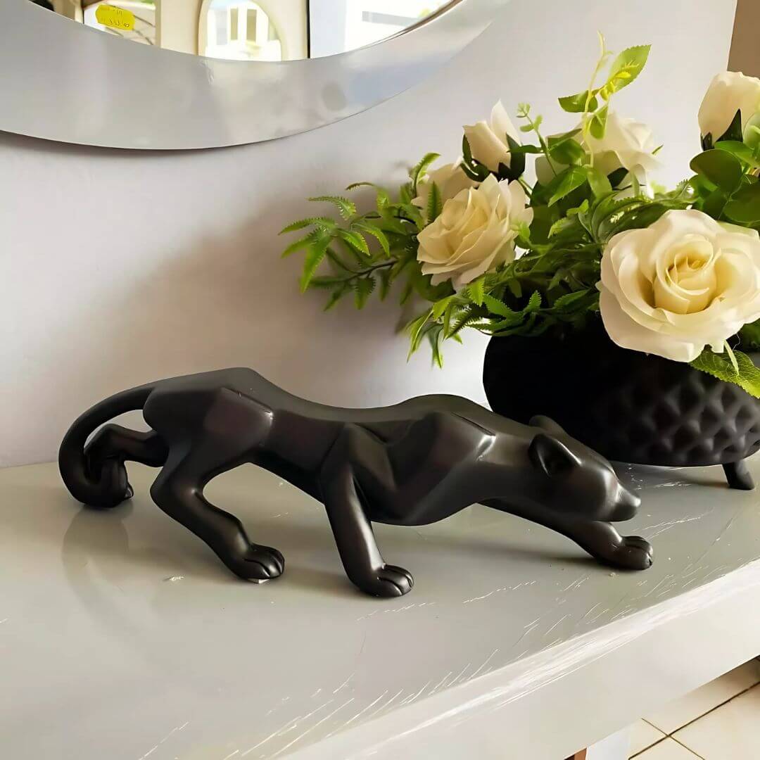 Enfeite pantera preta em destaque sobre aparador com plantas ao fundo

